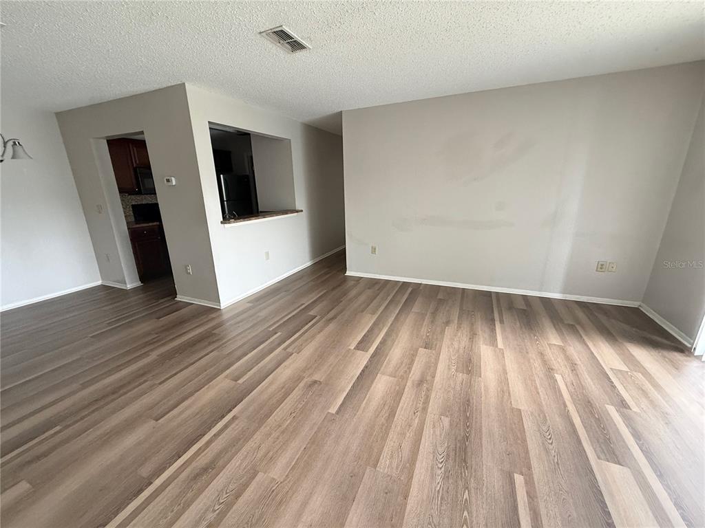 An empty living room features light-colored walls, wood-look flooring, and an opening to the kitchen — 3705 SW 27TH STREET UNIT 1026, GAINESVILLE, FL