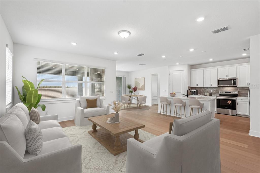 An open-concept living room and kitchen featuring light wood flooring and white cabinetry — 9927 JOHNSON OAKS GLEN, PARRISH, FL
