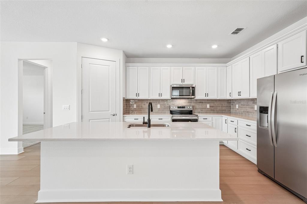 A modern kitchen features white cabinetry, a large quartz island, stainless steel appliances, and backsplash — 9927 JOHNSON OAKS GLEN, PARRISH, FL