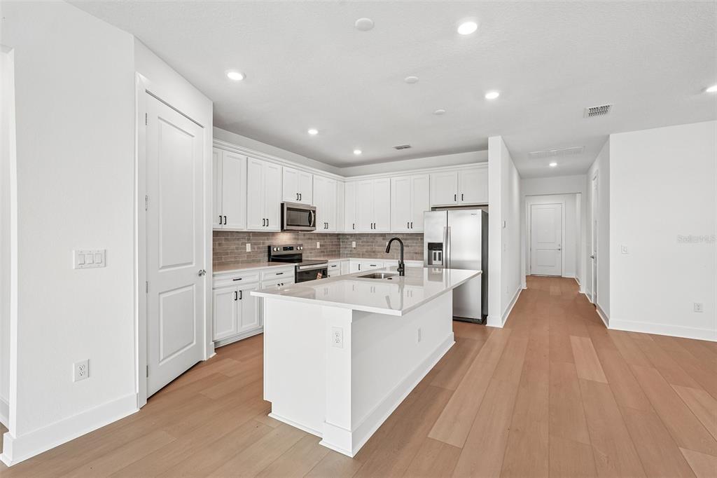 A modern kitchen features white cabinetry, a central island, stainless steel appliances, and wood flooring — 9927 JOHNSON OAKS GLEN, PARRISH, FL