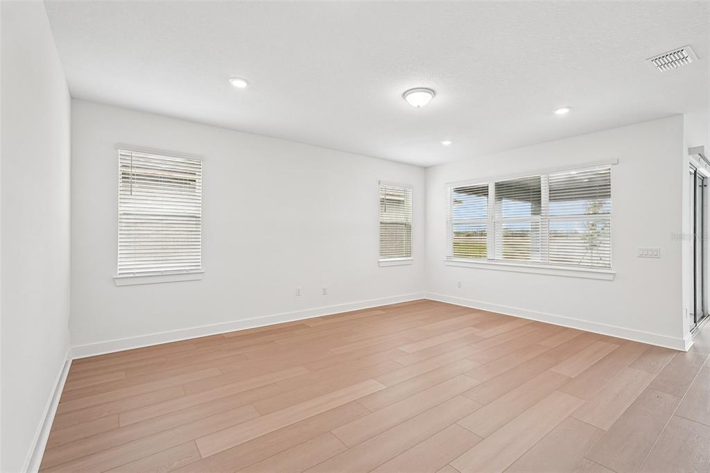 An empty room with white walls, light wood-look flooring, and several windows with blinds — 9927 JOHNSON OAKS GLEN, PARRISH, FL