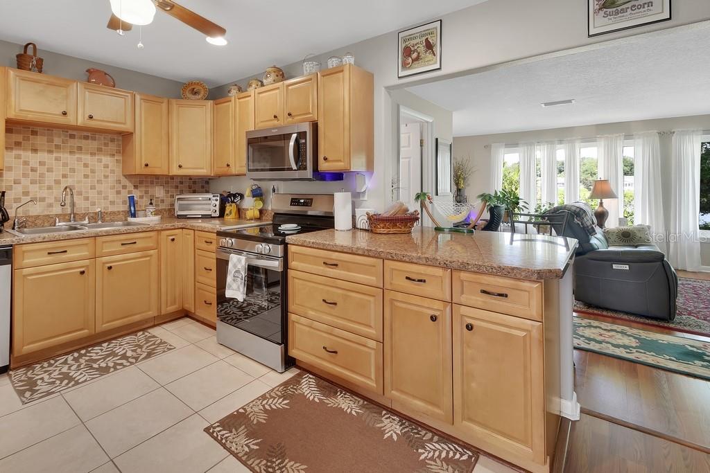 A kitchen with light wood cabinets, granite countertops, and a tile backsplash opens to a living area — 50 BONITA ROAD, DEBARY, FL