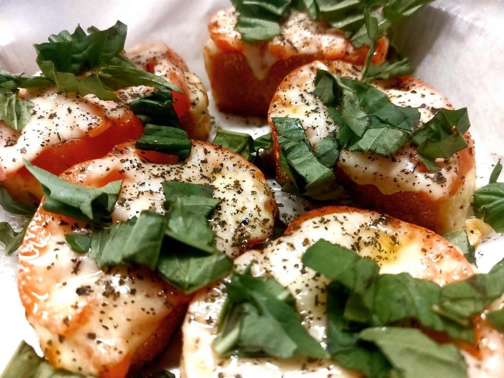 A close-up view of several toasted bread slices topped with melted cheese, herbs, and basil — 000 RESTAURANT AVENUE, FL