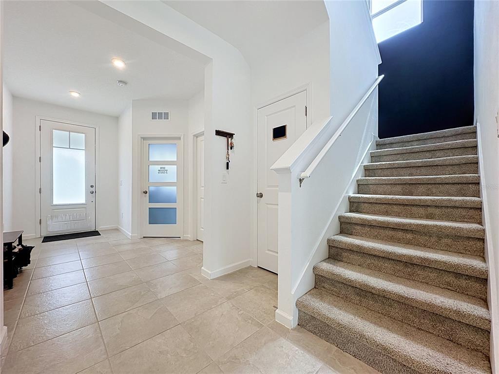 A tiled entryway features a front door, a staircase with carpet, and several interior doors — 900 HONEY PETAL LANE, DELAND, FL