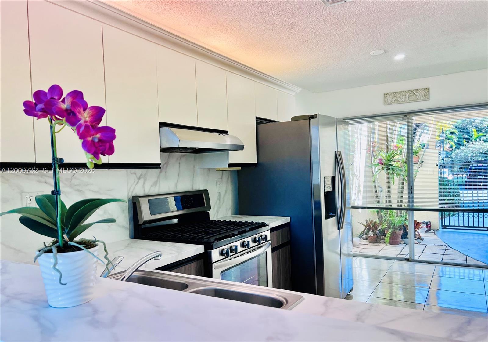 A kitchen features white cabinets, stainless steel appliances, marble-patterned countertops, and a sliding glass door — 4530 NW 102nd Ct, Doral FL 33178, DORAL, FL