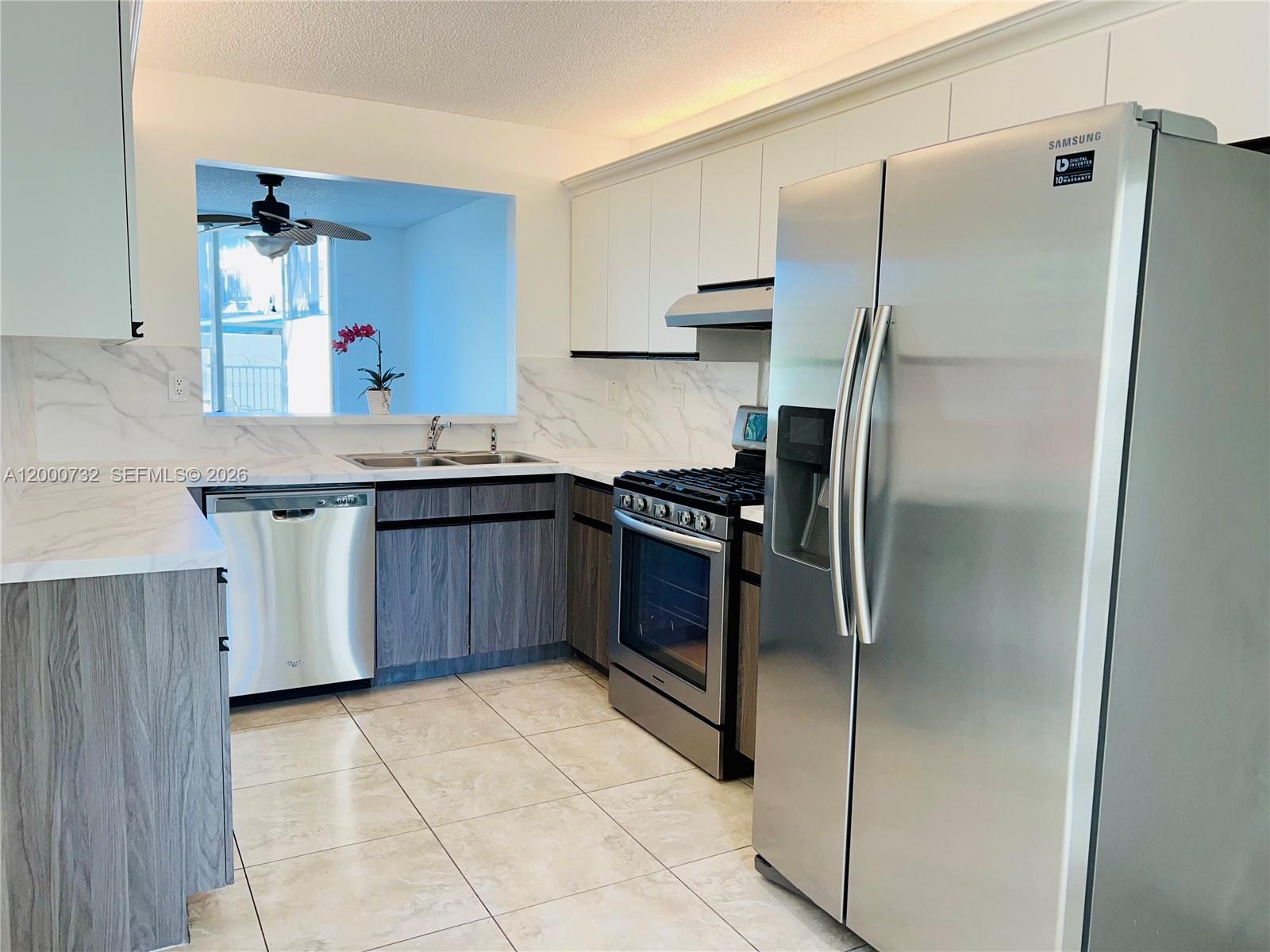 A kitchen features stainless steel appliances, wood-grain lower cabinets, white upper cabinets, and marble-look countertops — 4530 NW 102nd Ct, Doral FL 33178, DORAL, FL