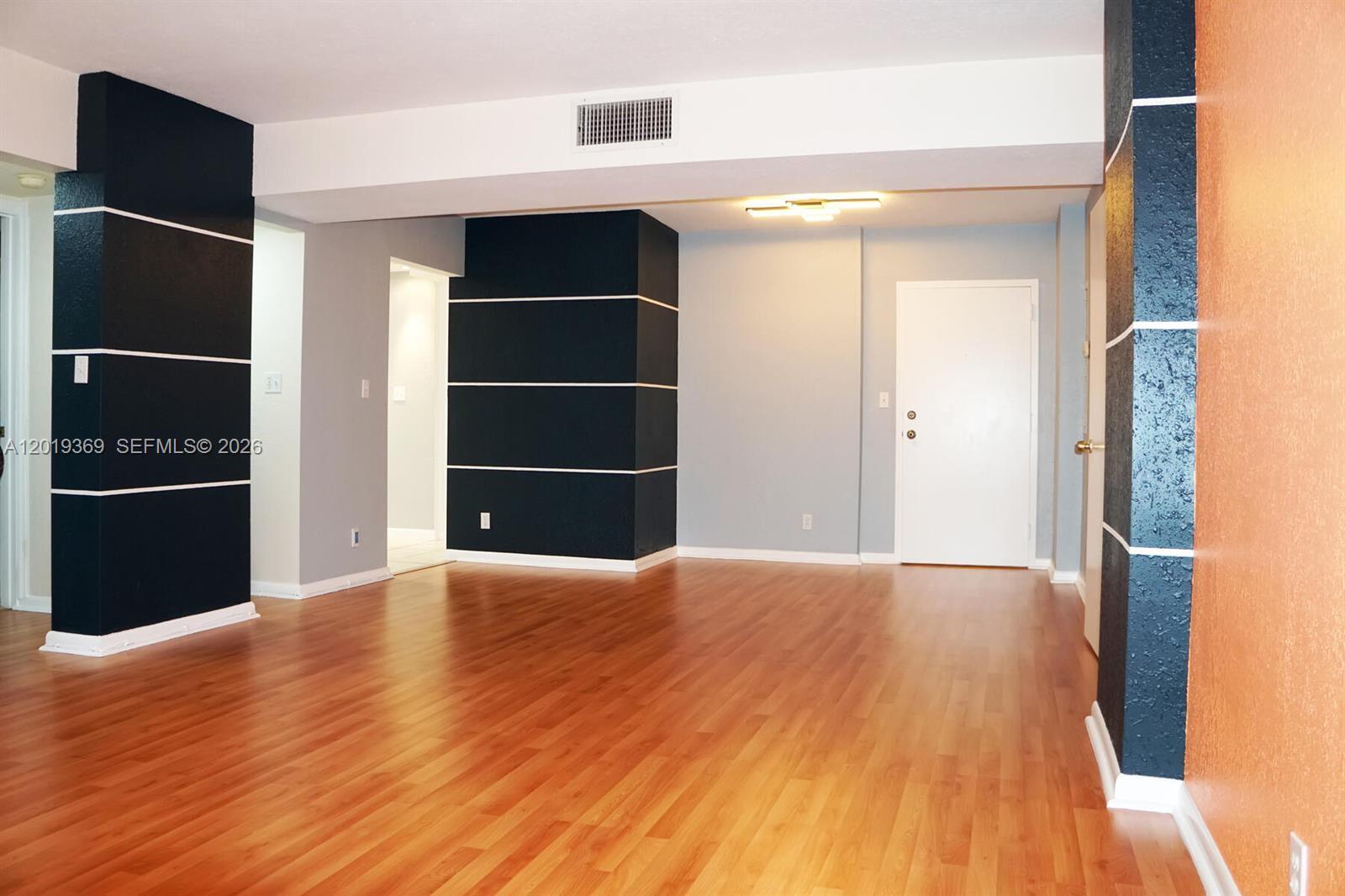 An empty room features wood-look flooring, light blue walls, and two dark accent pillars — 1900 Diana Dr # 3E, Hallandale Beach FL 33009, HALLANDALE BEACH, FL