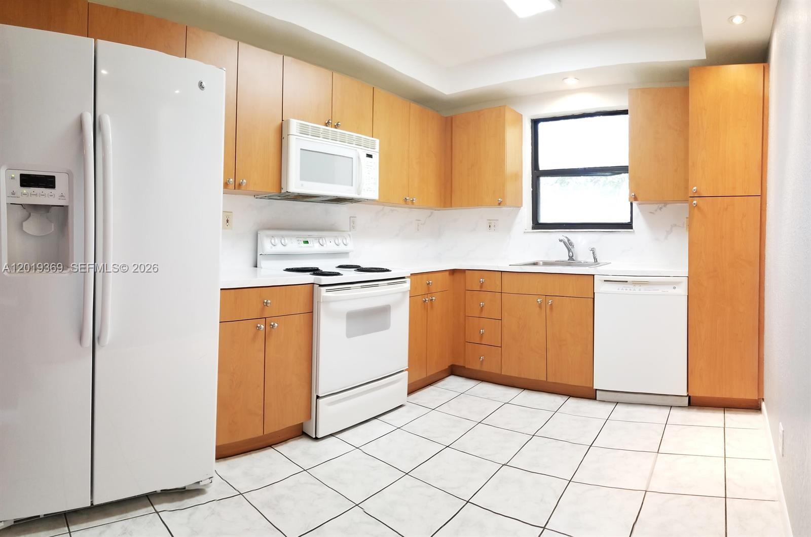 A kitchen features light wood cabinets, white appliances, white countertops, and white tiled flooring — 1900 Diana Dr # 3E, Hallandale Beach FL 33009, HALLANDALE BEACH, FL