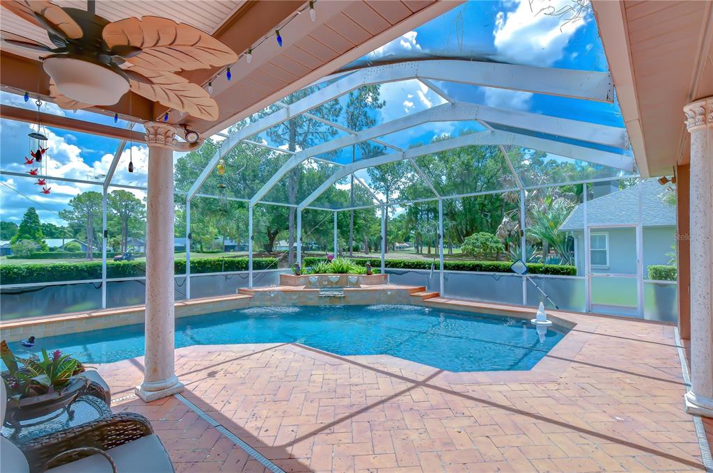 A screened-in patio features a swimming pool with a stone waterfall and brick paver flooring — 3810 TURKEY OAK DRIVE, VALRICO, FL