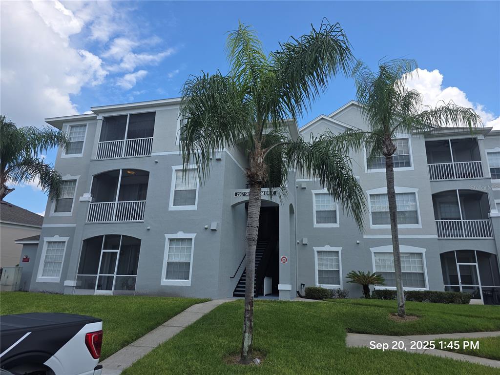 A three-story apartment building with gray stucco walls, screened balconies, and two palm trees — 2307 SILVER PALM DR UNIT 202, KISSIMMEE, FL