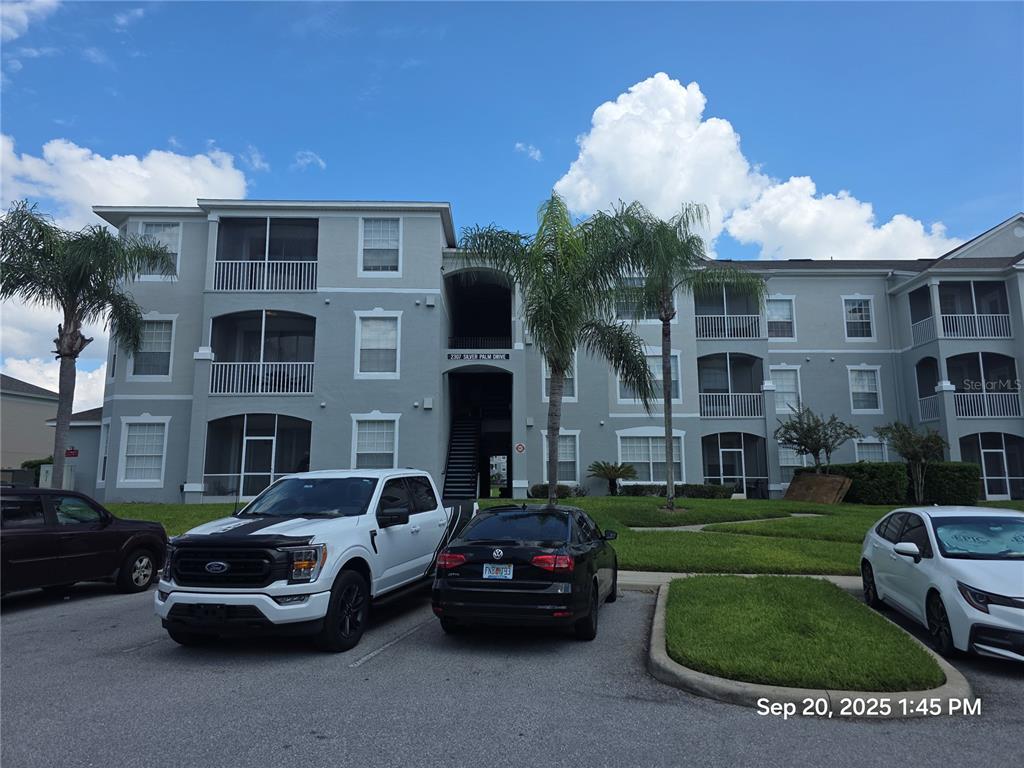 A three-story apartment building with a gray exterior, screened balconies, and a parking lot — 2307 SILVER PALM DR UNIT 202, KISSIMMEE, FL