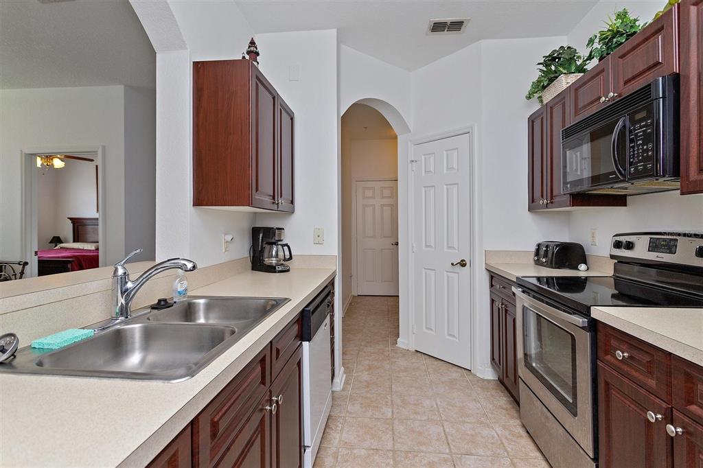 A kitchen features dark wood cabinets, stainless steel appliances, and beige countertops — 2307 SILVER PALM DR UNIT 202, KISSIMMEE, FL