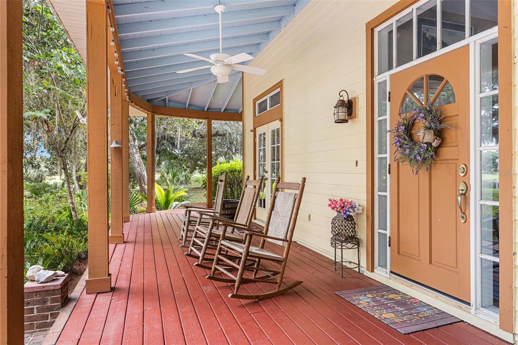 A covered wooden porch features three rocking chairs, a front door, and a ceiling fan — 33415 KIEFER ROAD, WESLEY CHAPEL, FL