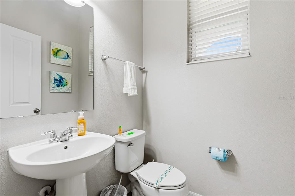 A small bathroom features a pedestal sink, a toilet, and two fish-themed wall art pieces — 5152 ADELAIDE DRIVE, KISSIMMEE, FL