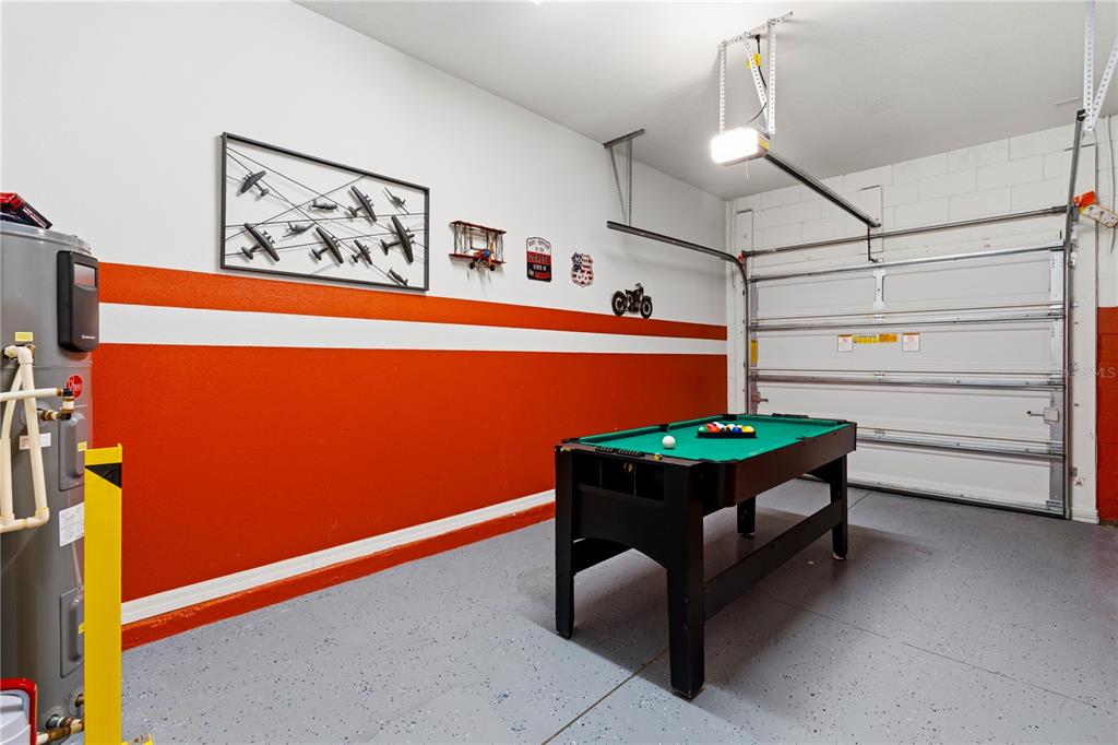 A garage with a pool table, painted orange and white walls, and a concrete floor — 5152 ADELAIDE DRIVE, KISSIMMEE, FL