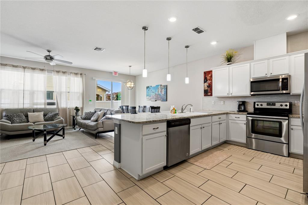 An open-concept kitchen and living area features white cabinetry, granite countertops, and tile flooring — 5152 ADELAIDE DRIVE, KISSIMMEE, FL