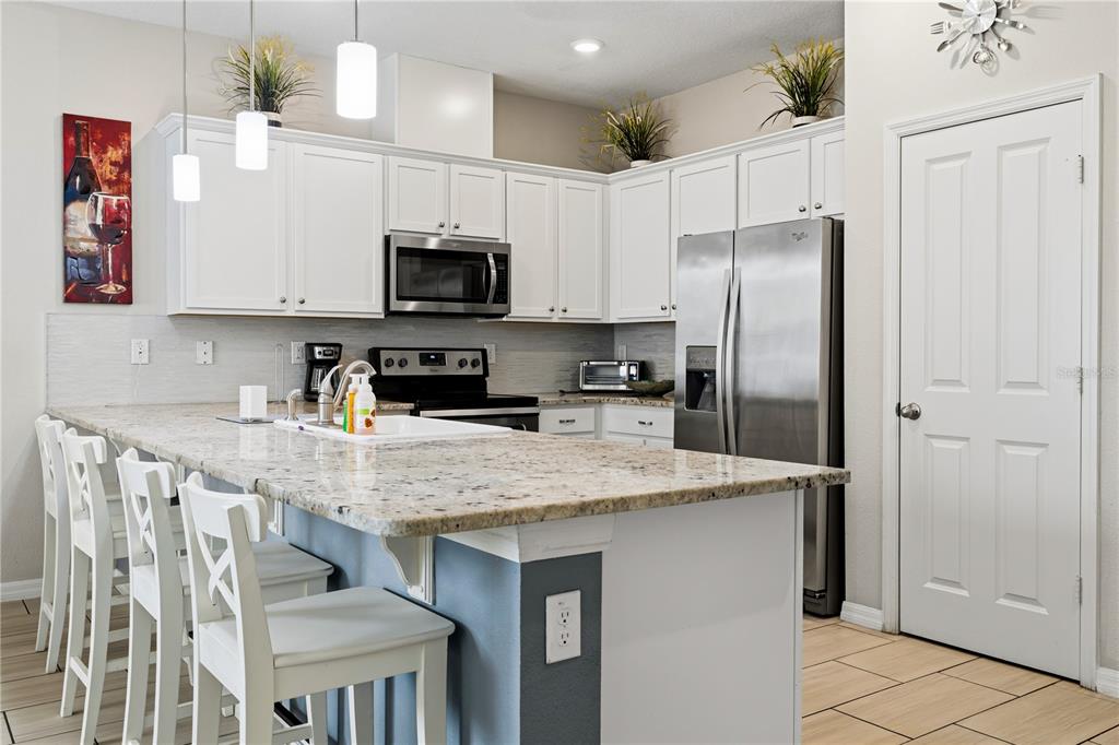 A kitchen features white cabinets, granite countertops, a large island with seating, and stainless appliances — 5152 ADELAIDE DRIVE, KISSIMMEE, FL