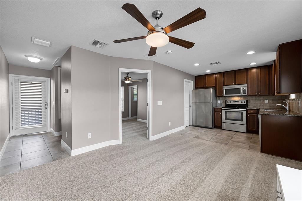 A living room with carpeted floors opens into a kitchen with dark wood cabinets — 8623 VIA TRIESTE, WINDERMERE, FL