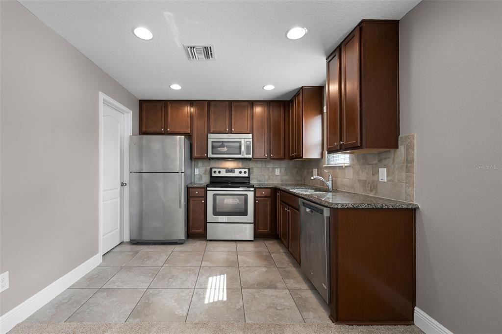 A kitchen features dark wood cabinets, stainless steel appliances, granite countertops, and tiled flooring — 8623 VIA TRIESTE, WINDERMERE, FL