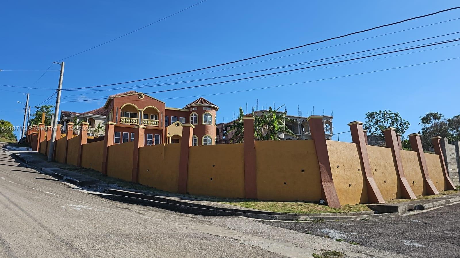 A large, multi-story house with a turret stands behind a tall, yellow perimeter wall — 00 Heavenly Heights Hanover,Jamaica, NA, NA