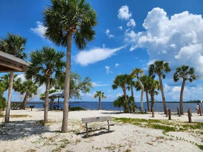 A sandy beach area features palm trees, a wooden bench, and a view of water — 20339 BACHMANN BOULEVARD, PORT CHARLOTTE, FL