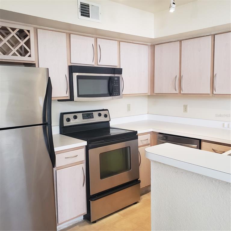 A kitchen with light wood cabinets, stainless steel appliances, and white countertops — 7280 WESTPOINTE BOULEVARD UNIT 831, ORLANDO, FL