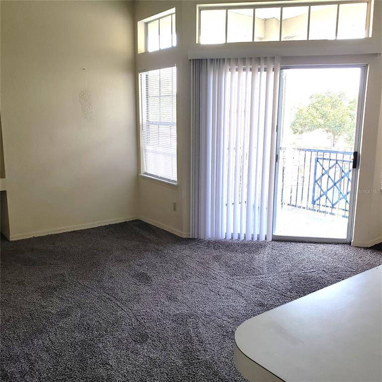 A living room with gray carpet, a sliding glass door, and windows with blinds — 7280 WESTPOINTE BOULEVARD UNIT 831, ORLANDO, FL