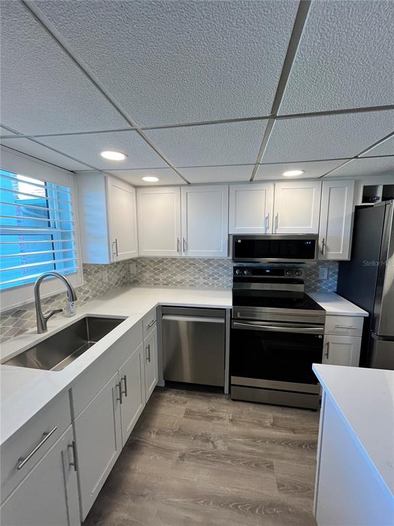A kitchen features white cabinets, stainless steel appliances, a tile backsplash, and light wood flooring — 2727 75TH STREET W UNIT 7A14, BRADENTON, FL