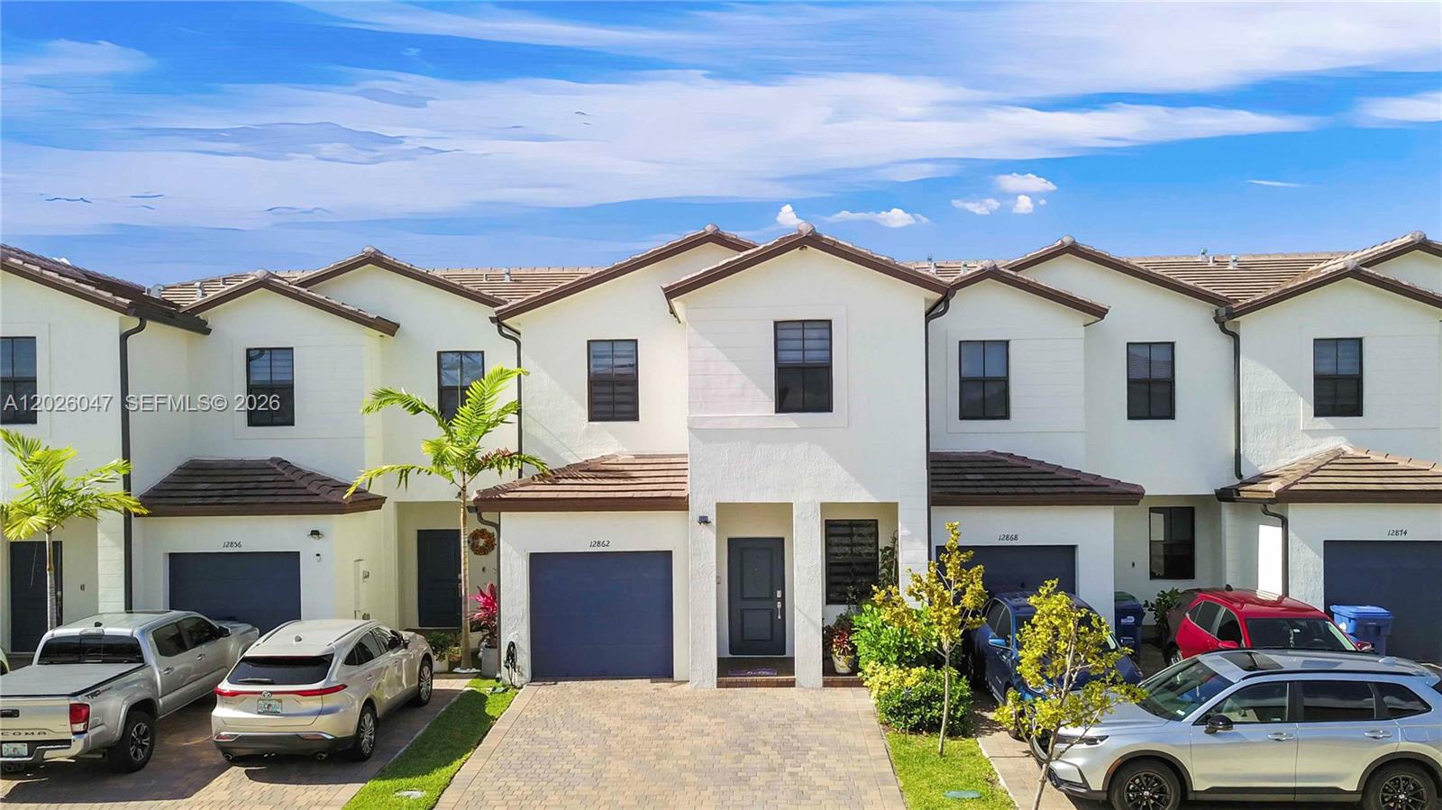 A row of two-story townhouses features white stucco facades, dark garage doors, and paved driveways — 12862 SW 231st St, Miami FL 33170, MIAMI, FL