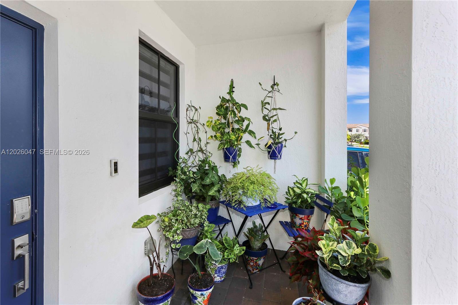 A small covered porch features a blue bistro set surrounded by numerous potted plants — 12862 SW 231st St, Miami FL 33170, MIAMI, FL