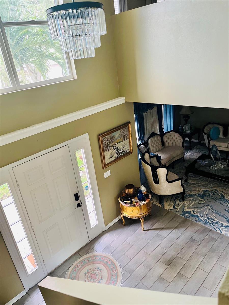 An elevated view of a foyer with a chandelier, front door, and adjacent living area — 184 Massini Avenue NW, Palm Bay FL 32907, PALM BAY, FL