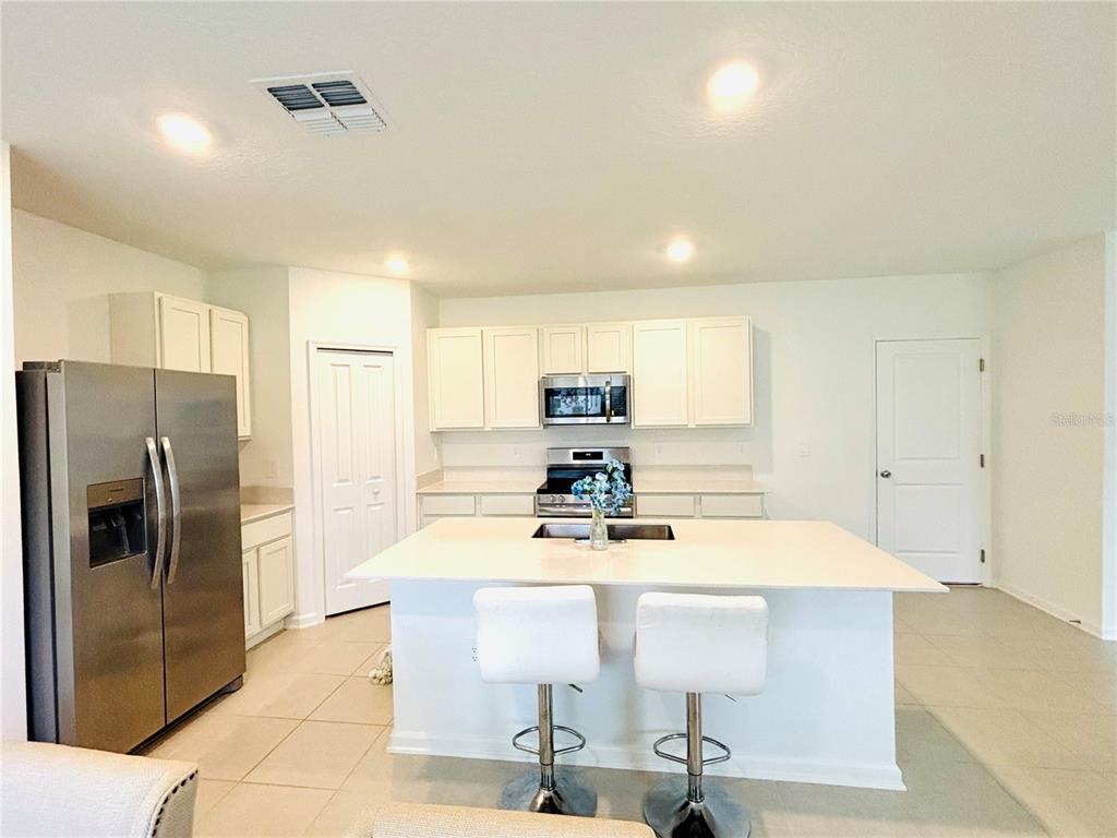 A kitchen features white cabinets, stainless steel appliances, a central island, and two bar stools — 4045 OLD MILL ROAD, HAINES CITY, FL
