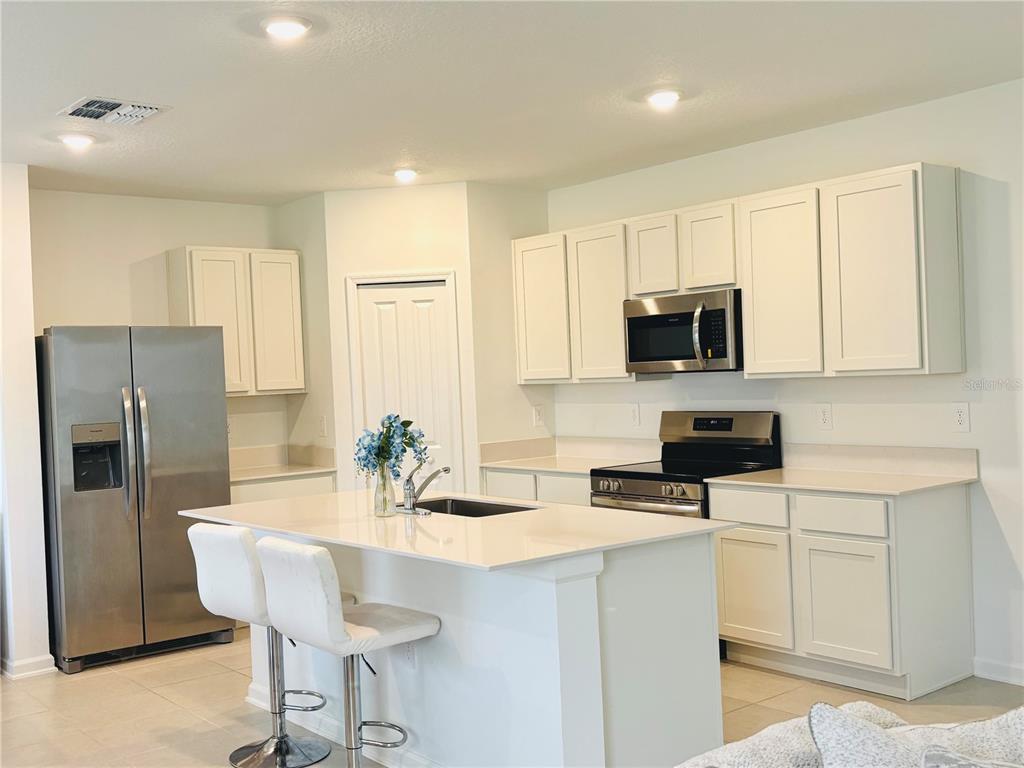 A modern kitchen features white cabinetry, stainless steel appliances, and a central island with seating — 4045 OLD MILL ROAD, HAINES CITY, FL