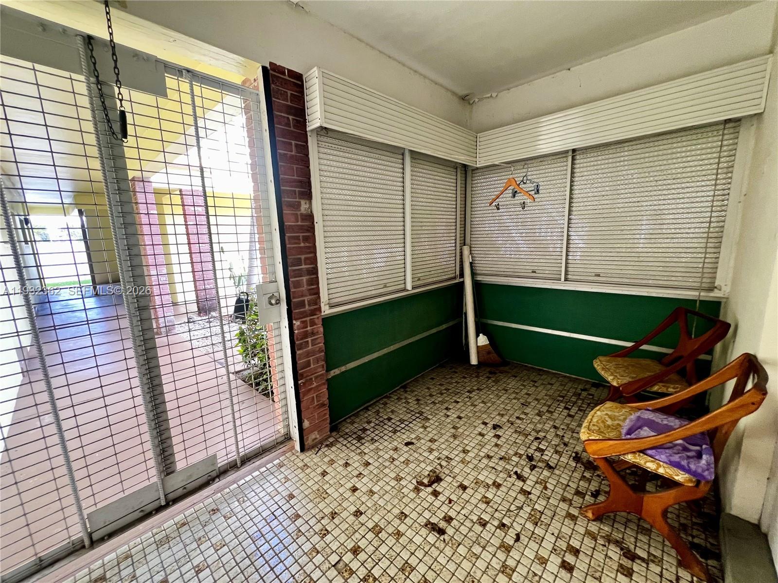 A sunroom features tiled flooring, green walls, two wooden chairs, and a metal security gate — 1501 Arthur St # 5, Hollywood FL 33020, HOLLYWOOD, FL