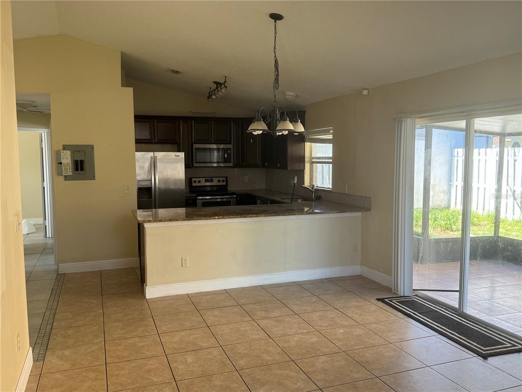 A kitchen with dark cabinets, granite countertops, and tile flooring opens to a dining area — 2399 HARBOR TOWN DRIVE, KISSIMMEE, FL