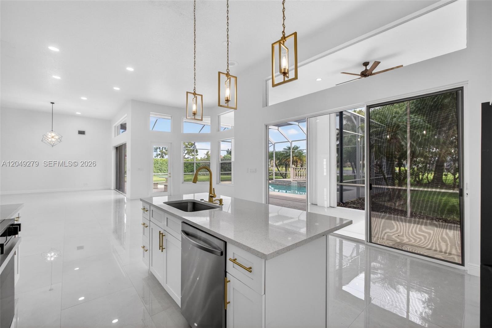 A modern kitchen island with a sink and gold hardware sits before a pool view — 19558 Red Gum Trl, Jupiter FL 33458, JUPITER, FL