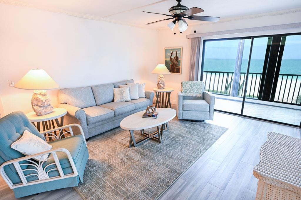 A living room features a grey sofa, armchairs, and a sliding door overlooking the ocean — 1100 BENJAMIN FRANKLIN DRIVE UNIT 502, SARASOTA, FL