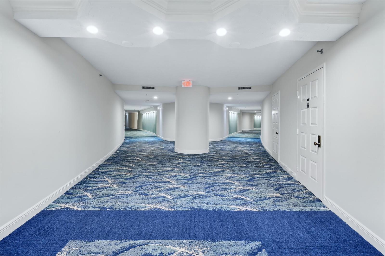 A wide hotel hallway features a central pillar, white walls, and blue patterned carpeting — 1300 S Highway A1a # 320, Jupiter FL 33477, JUPITER, FL