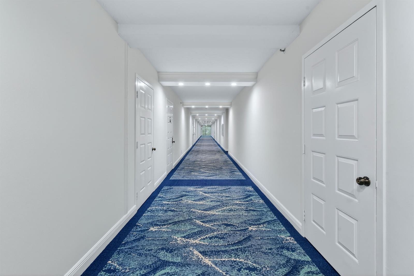 A long, narrow hotel hallway with white walls, white doors, and blue patterned carpeting — 1300 S Highway A1a # 320, Jupiter FL 33477, JUPITER, FL