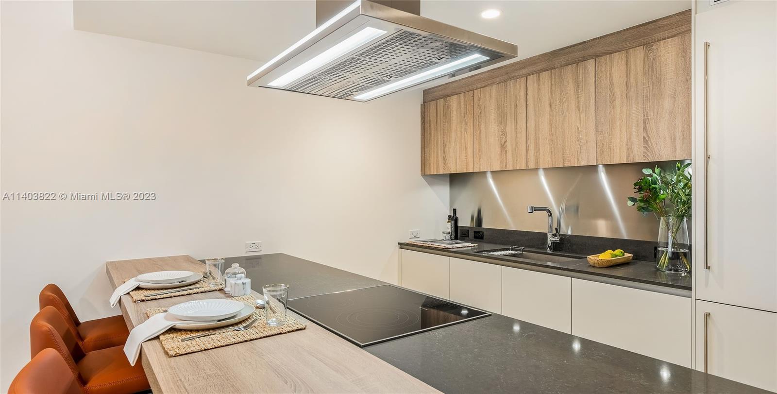 A modern kitchen features a large island with a cooktop, wood cabinetry, and stainless backsplash — 1000 Brickell Plaza # 2711, Miami FL 33131, MIAMI, FL