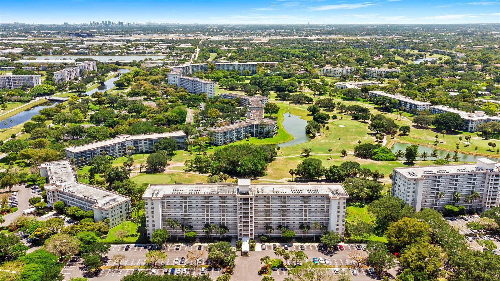 An aerial view shows several multi-story apartment buildings surrounded by green lawns and golf course ponds — 3510 Oaks Way # 1002, Pompano Beach FL 33069, POMPANO BEACH, FL