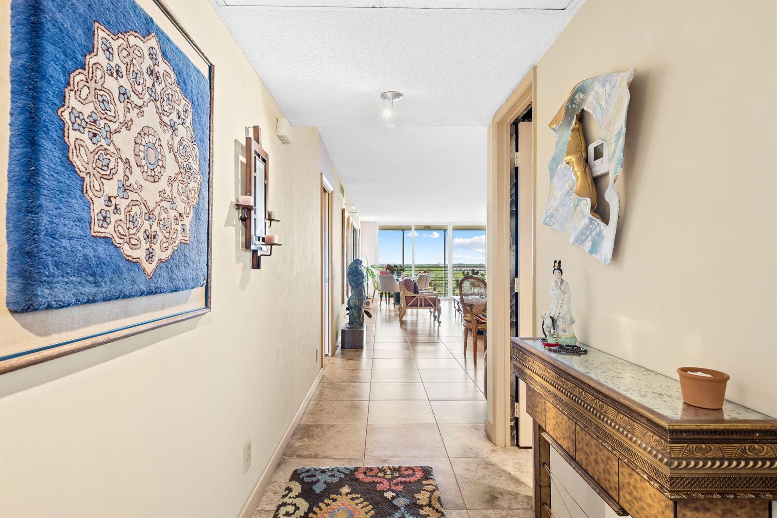 A hallway with tile flooring leads toward a living area with floor-to-ceiling windows — 3510 Oaks Way # 1002, Pompano Beach FL 33069, POMPANO BEACH, FL