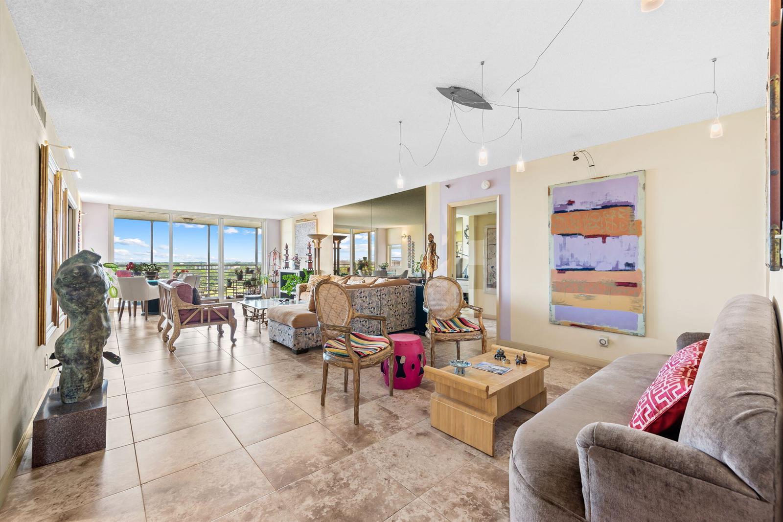 A spacious living room features tile flooring, a large abstract painting, and floor-to-ceiling windows — 3510 Oaks Way # 1002, Pompano Beach FL 33069, POMPANO BEACH, FL