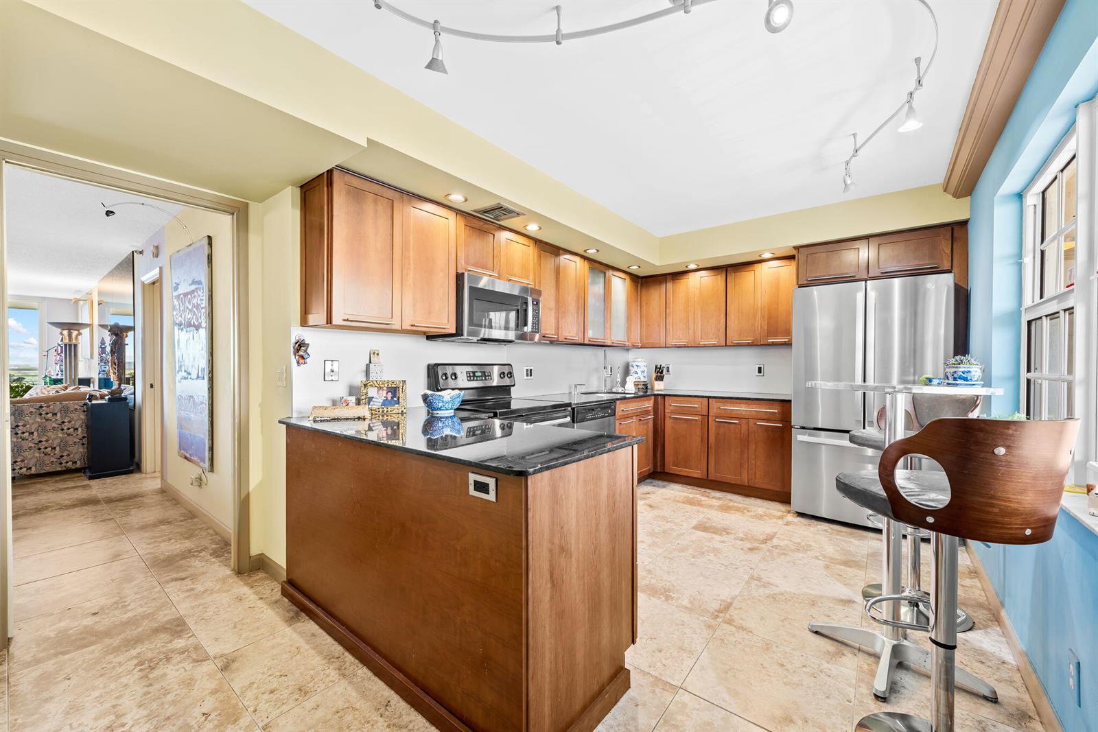 A kitchen features wooden cabinets, black granite countertops, stainless steel appliances, and tile flooring — 3510 Oaks Way # 1002, Pompano Beach FL 33069, POMPANO BEACH, FL