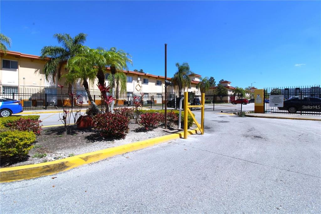 A gated entrance leads to a multi-story apartment building with palm trees and landscaping — 746 MCDOUGALL COURT UNIT 746, ORLANDO, FL