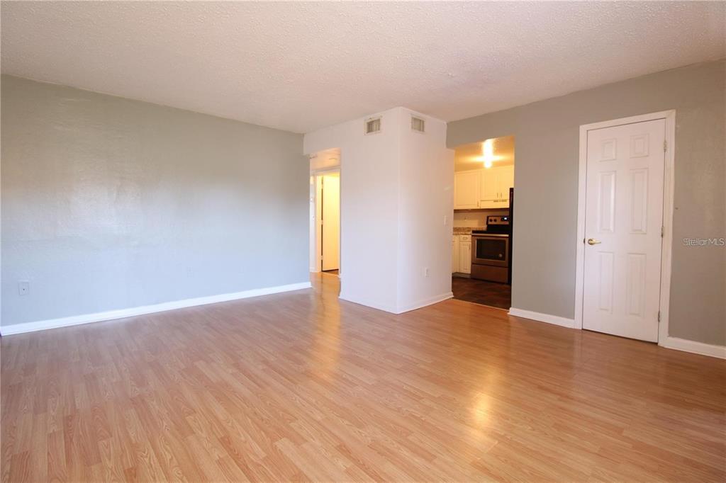 An empty room with light wood-look flooring, gray walls, and an adjacent kitchen — 746 MCDOUGALL COURT UNIT 746, ORLANDO, FL