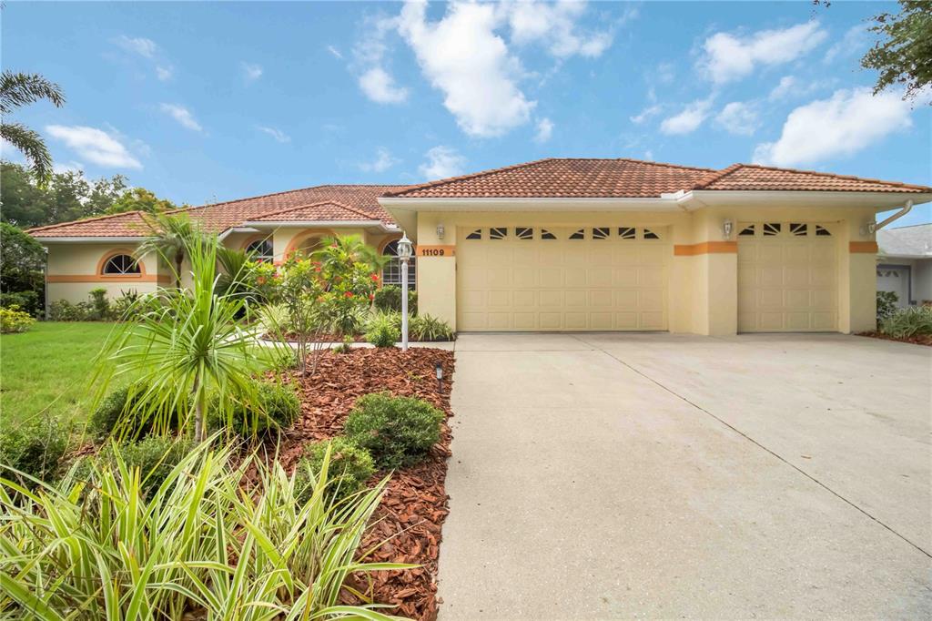 A single-story house with a yellow stucco exterior, a tile roof, and a three-car garage — 11109 28TH STREET CIRCLE E, PARRISH, FL