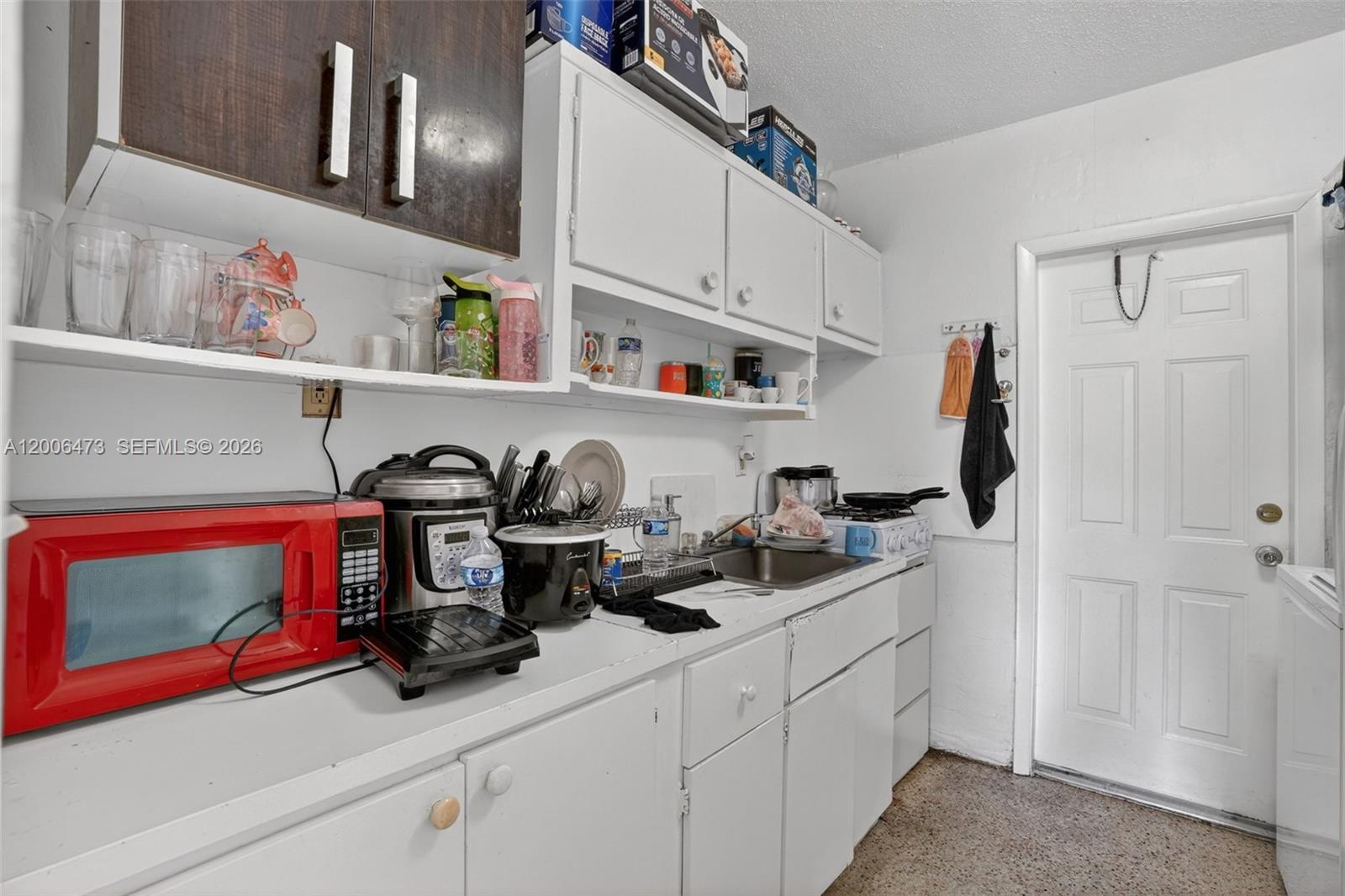 A small kitchen features white cabinets, a red microwave, and a stainless steel sink — 2110 NW 24th St, Miami FL 33142, MIAMI, FL