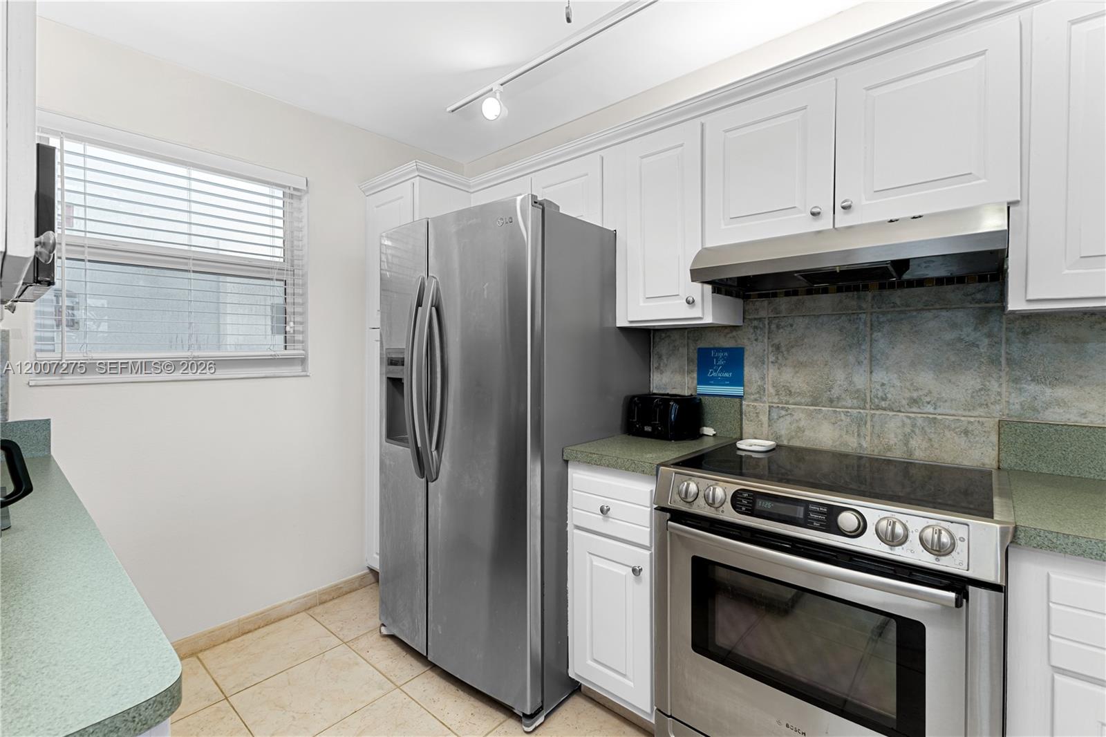 A kitchen features white cabinets, stainless steel appliances, green countertops, and a tile backsplash — 1391 S Ocean Blvd # 409, Pompano Beach FL 33062, POMPANO BEACH, FL