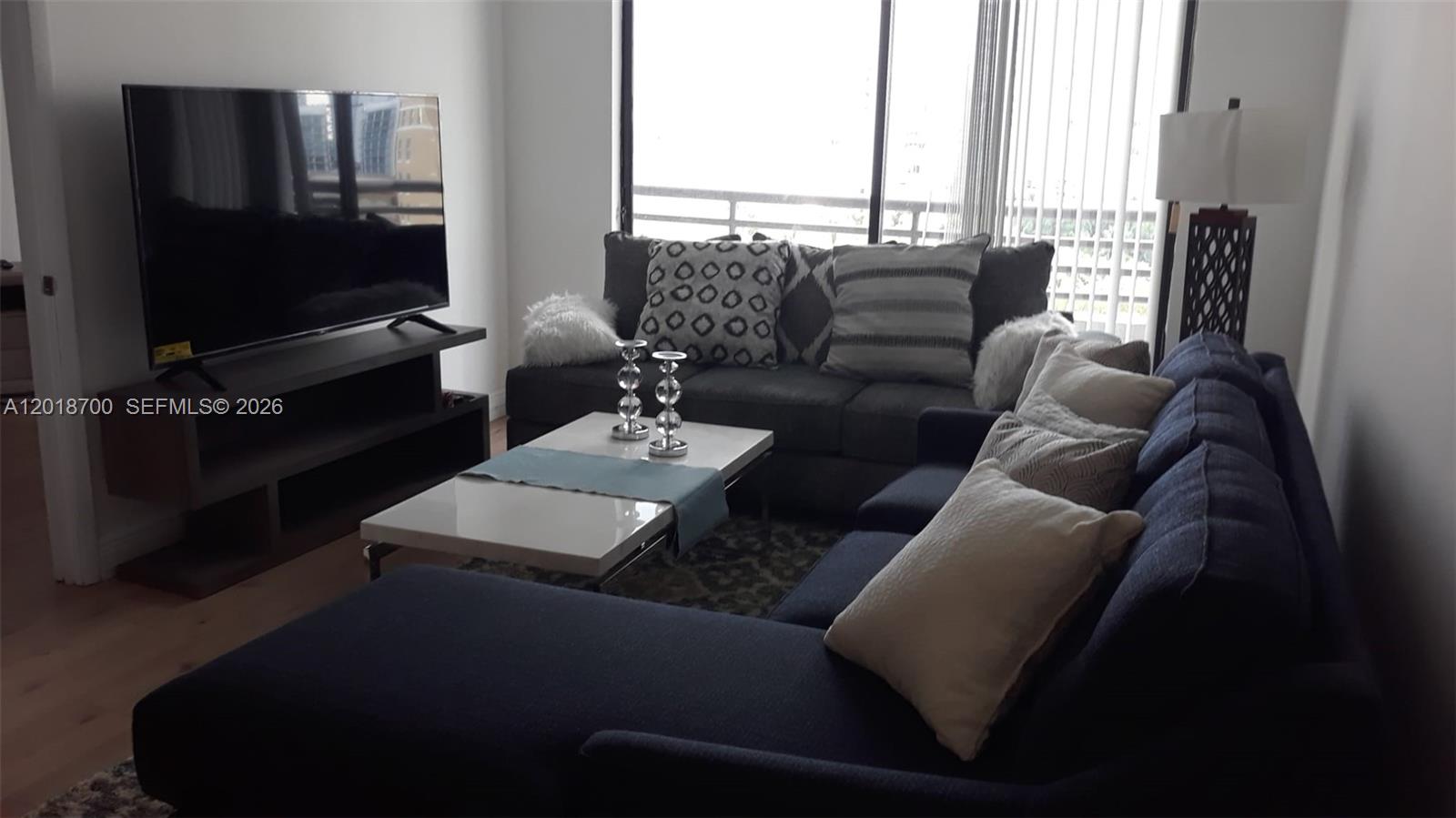 A living room features a dark sectional sofa, a white coffee table, and a television — AVENTURA, FL